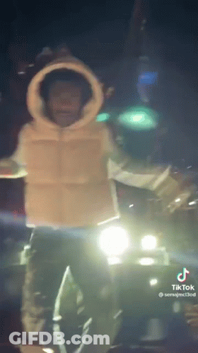 A Man Is Standing In Front Of A Car At Night . GIF