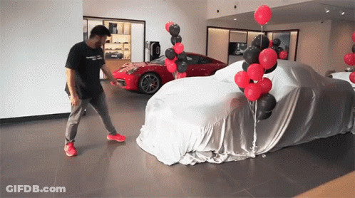 A Man Is Standing In Front Of A Car Covered In A Cloth GIF