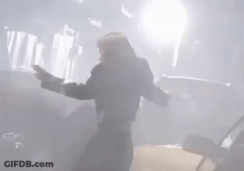 A Man Is Standing In Front Of A Car With His Arms Outstretched In A Foggy Room . GIF