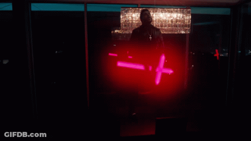 A Man Is Standing In Front Of A Chandelier And Holding A Red Light That Says - = + GIF