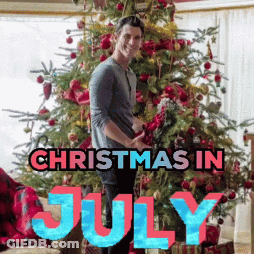 A Man Is Standing In Front Of A Christmas Tree With The Words Christmas In July Above Him GIF