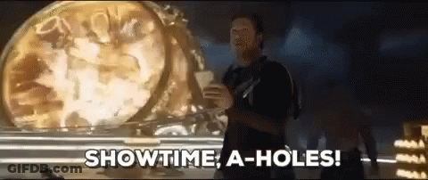 A Man Is Standing In Front Of A Clock And Says Showtime A-Holes GIF