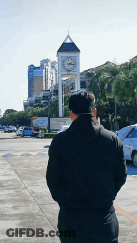 A Man Is Standing In Front Of A Clock Tower That Says ' A ' On It GIF
