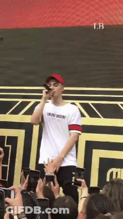 A Man Is Standing In Front Of A Crowd Holding A Microphone GIF