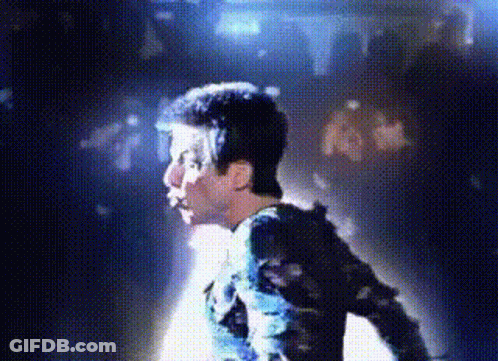 A Man Is Standing In Front Of A Crowd In A Dark Room With Blue Lights Behind Him . GIF