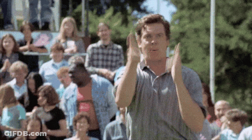 A Man Is Standing In Front Of A Crowd Of People And Applauding . GIF