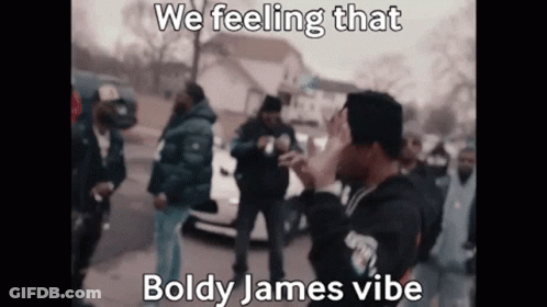 A Man Is Standing In Front Of A Crowd Of People And Covering His Face . GIF