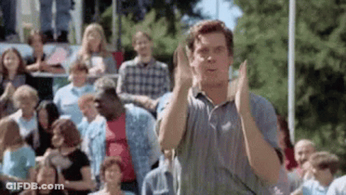 A Man Is Standing In Front Of A Crowd Of People Clapping His Hands . GIF