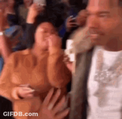 A Man Is Standing In Front Of A Crowd Of People Holding A Cell Phone . GIF