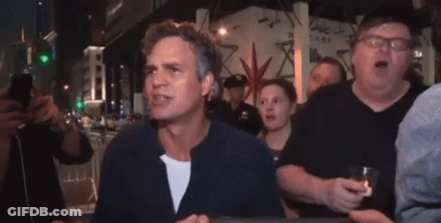 A Man Is Standing In Front Of A Crowd Of People Holding A Glass Of Beer . GIF