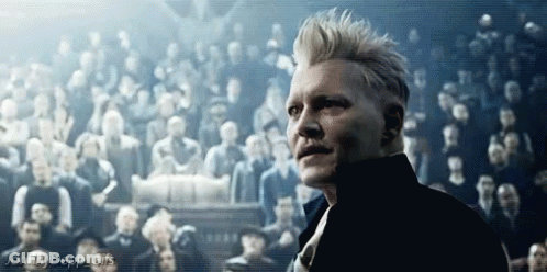 A Man Is Standing In Front Of A Crowd Of People In A Dark Room . GIF