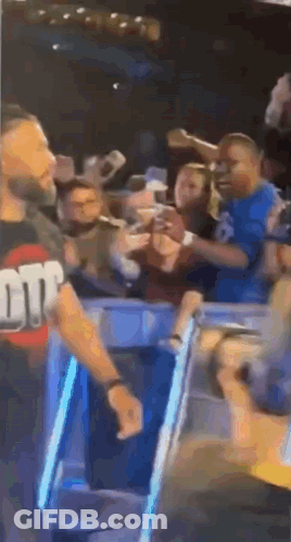 A Man Is Standing In Front Of A Crowd Of People In A Stadium . GIF