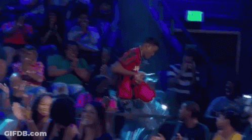 A Man Is Standing In Front Of A Crowd Of People In A Stadium . GIF