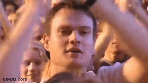 A Man Is Standing In Front Of A Crowd Of People With His Hands In The Air At A Concert . GIF