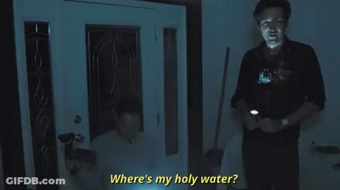 A Man Is Standing In Front Of A Door Holding A Flashlight And Asking Where Is My Holy Water . GIF