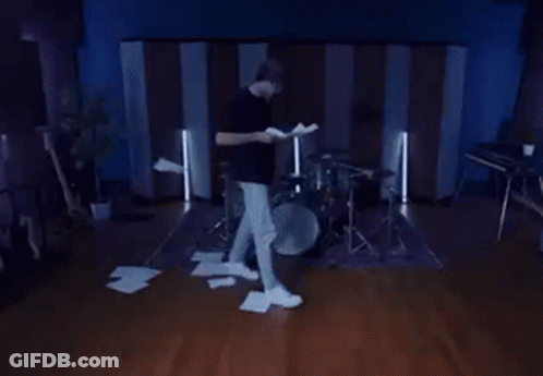 A Man Is Standing In Front Of A Drum Set Holding A Piece Of Paper GIF