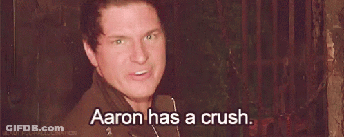 A Man Is Standing In Front Of A Fence And Saying `` Aaron Has A Crush '' . GIF