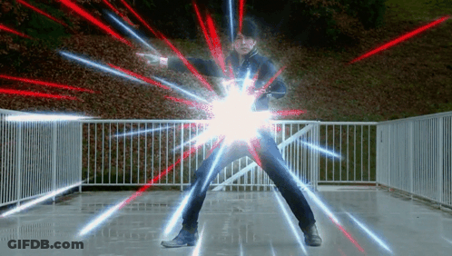 A Man Is Standing In Front Of A Fence With Red And Blue Lights Coming Out Of His Arms . GIF