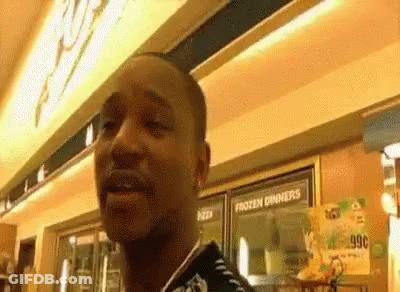 A Man Is Standing In Front Of A Frozen Dinners Sign In A Store . GIF