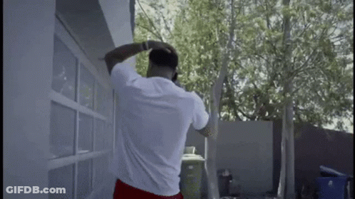 A Man Is Standing In Front Of A Garage Door Talking On A Cell Phone . GIF