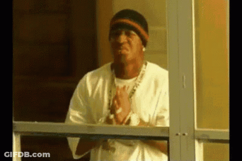 A Man Is Standing In Front Of A Glass Door With His Hands Folded . GIF