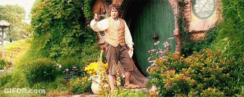 A Man Is Standing In Front Of A Green Door In A Garden Holding A Sword . GIF