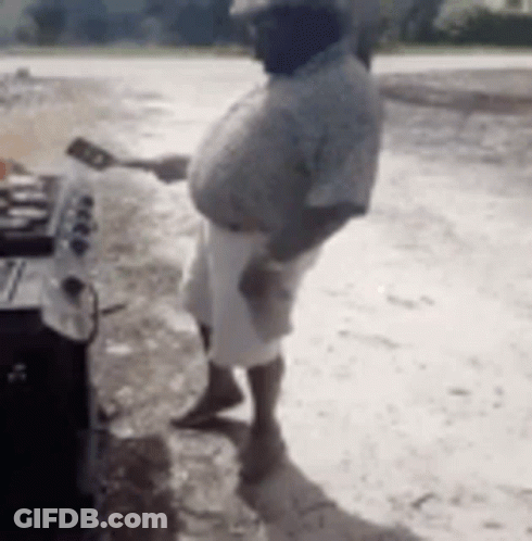 A Man Is Standing In Front Of A Grill Holding A Spatula And A Spoon . GIF