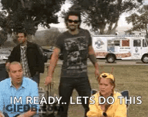 A Man Is Standing In Front Of A Group Of People While A Woman Sits In A Chair . GIF