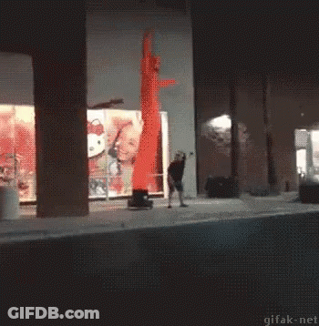 A Man Is Standing In Front Of A Hello Kitty Sign And A Red Air Dancer GIF