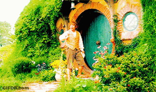 A Man Is Standing In Front Of A Hobbit House In The Woods . GIF