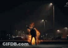 A Man Is Standing In Front Of A Huge Explosion Of Fire . GIF