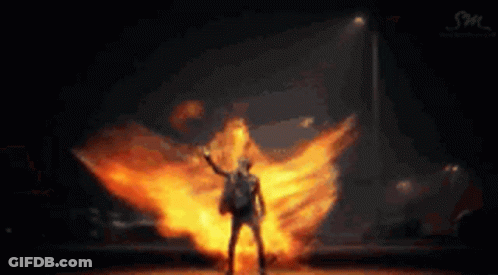 A Man Is Standing In Front Of A Huge Explosion Of Fire . GIF