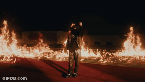 A Man Is Standing In Front Of A Large Amount Of Flames GIF