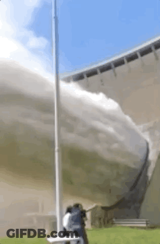A Man Is Standing In Front Of A Large Building With A Hose Spraying Water . GIF