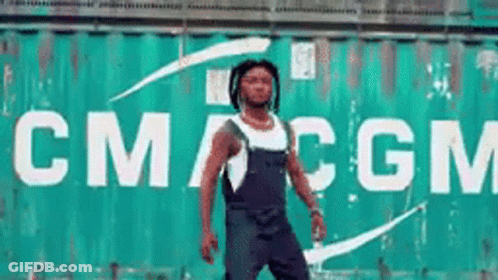 A Man Is Standing In Front Of A Large Green Container That Says Cmcgm GIF