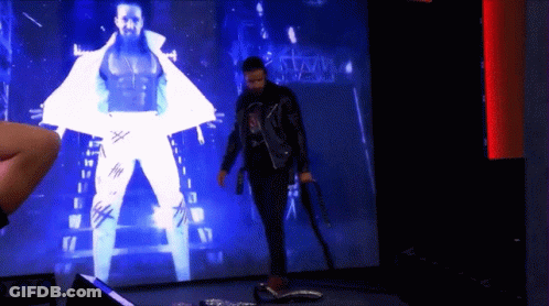 A Man Is Standing In Front Of A Large Screen That Says Wwe GIF