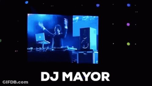A Man Is Standing In Front Of A Large Screen With The Word Dj Mayor On It . GIF