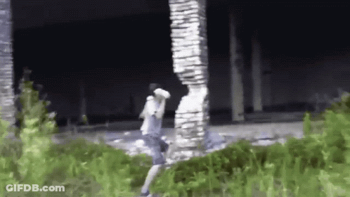 A Man Is Standing In Front Of A Large Stone Pillar In A Field . GIF