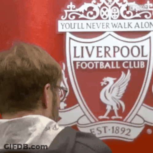 A Man Is Standing In Front Of A Liverpool Football Club Logo . GIF