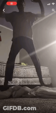 A Man Is Standing In Front Of A Mattress In A Room . GIF
