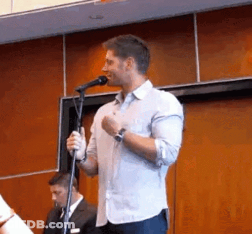 A Man Is Standing In Front Of A Microphone And Talking Into It . GIF