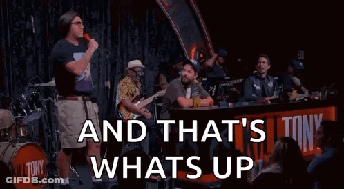 A Man Is Standing In Front Of A Microphone On A Stage With A Band Behind Him . GIF