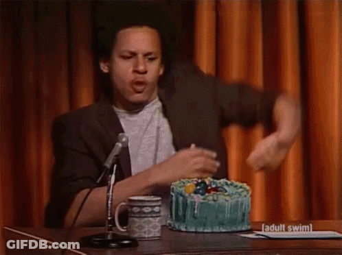 A Man Is Standing In Front Of A Microphone With A Cake In Front Of Him That Says Adult Swim On It GIF