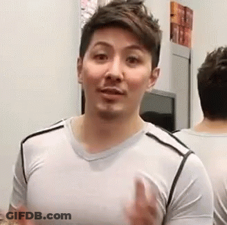 A Man Is Standing In Front Of A Mirror Wearing A White Shirt And Making A Funny Face . GIF