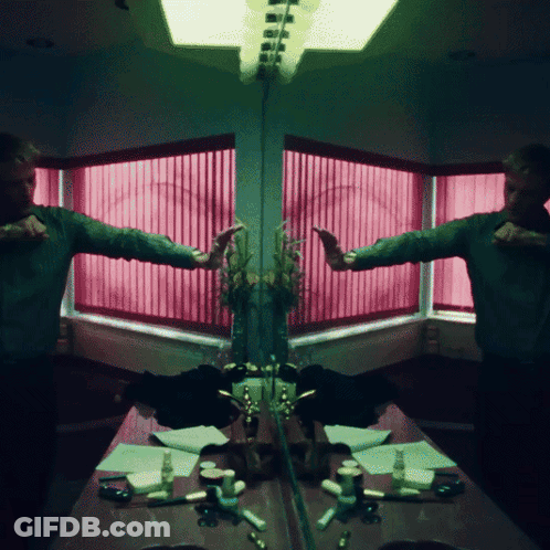 A Man Is Standing In Front Of A Mirror With A Pink Window Behind Him GIF