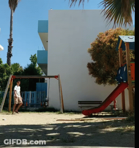 A Man Is Standing In Front Of A Playground With A Slide And Swings GIF