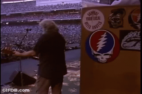 A Man Is Standing In Front Of A Podium With A Grateful Dead Sticker On It In A Stadium . GIF