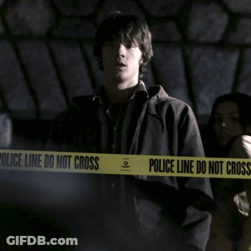 A Man Is Standing In Front Of A Police Line Do Not Cross Tape GIF