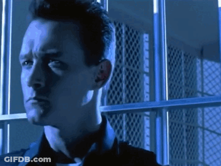 A Man Is Standing In Front Of A Prison Cell With Bars GIF