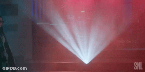A Man Is Standing In Front Of A Projector Screen In A Dark Room With A Red Background . GIF